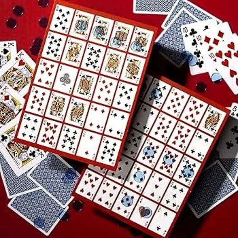Two game boards filled with playing cards, surrounded by loose cards and red tokens on a red table.