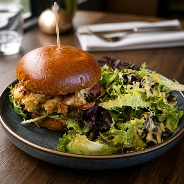Crab cake sandwich on a brioche bun with a side of mixed green salad and dressing.